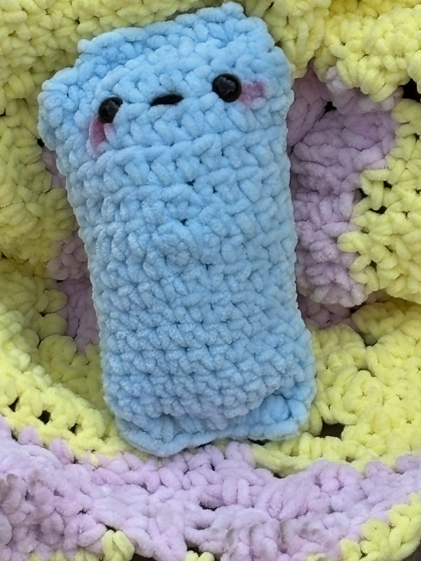 Light blue chunky crochet pocket plush on a pastel blanket