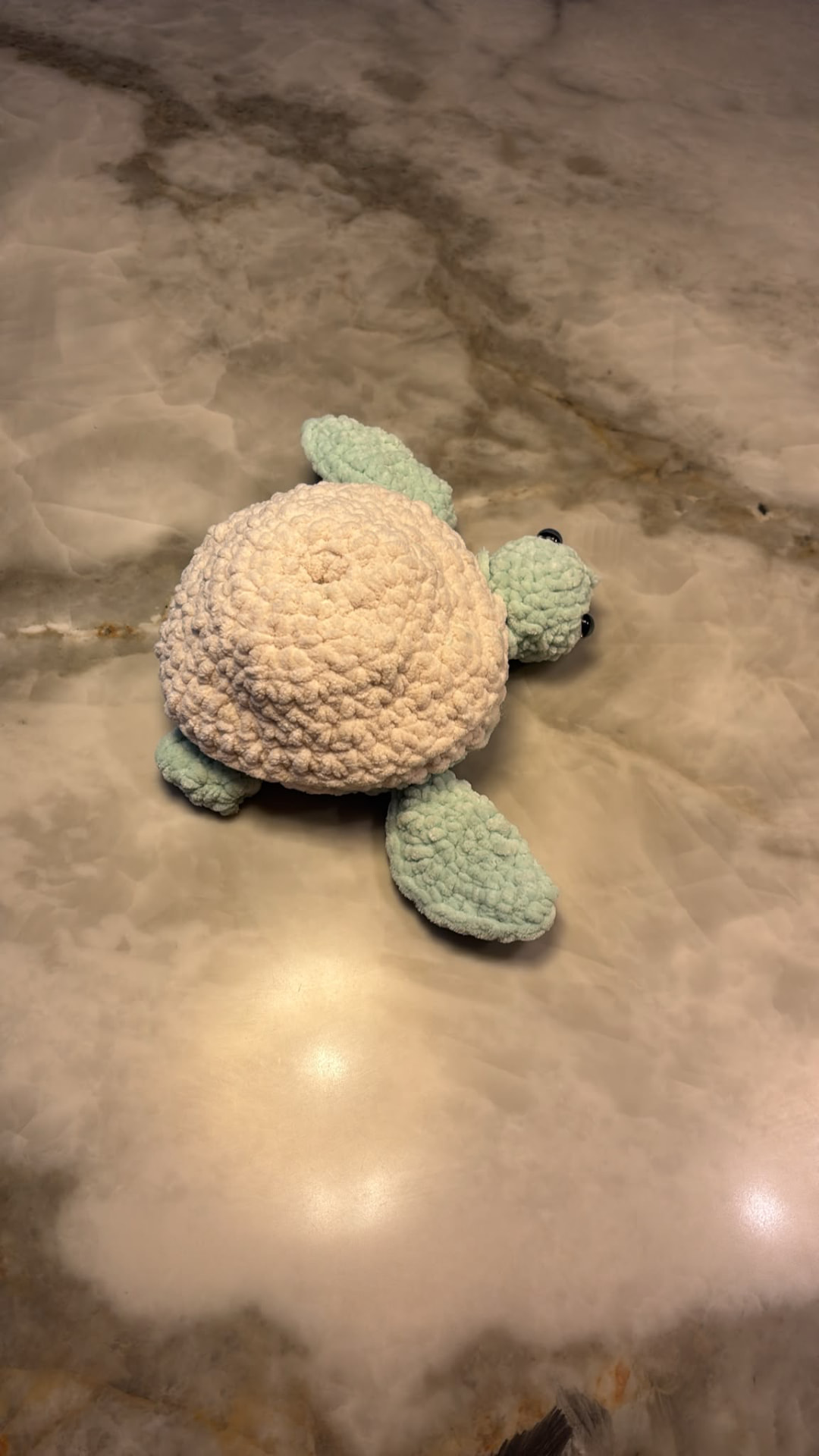 Chunky crochet turtle with a cream shell and mint green head and flippers on a marble surface