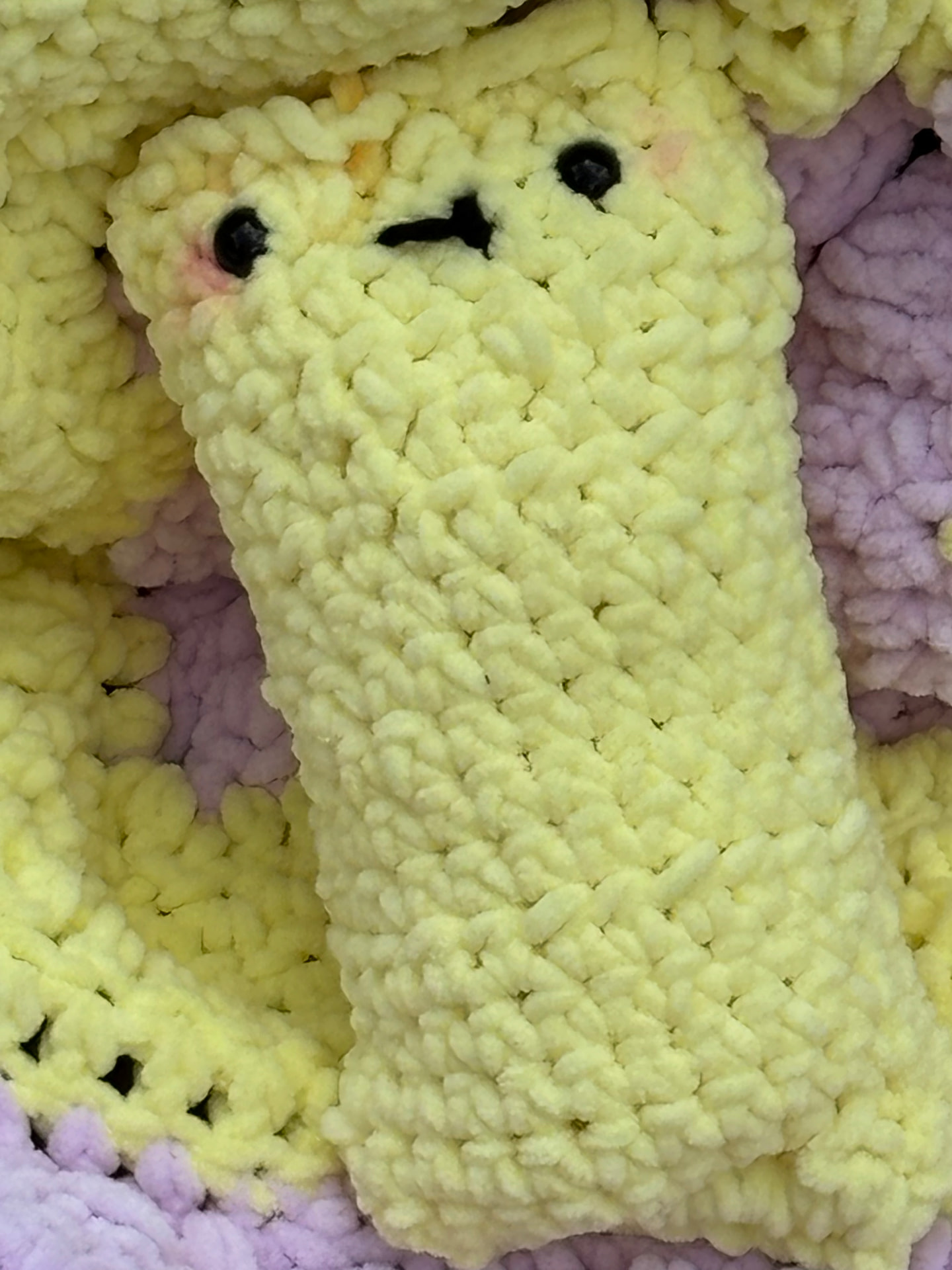 Pale yellow chunky crochet pocket plush resting on a pastel blanket